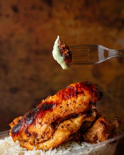 Poulet grillé épicé servi avec du riz blanc, un morceau de poulet trempé dans une sauce crémeuse sur une fourchette.