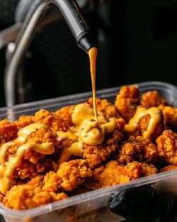 Des morceaux de poulet frit croustillants, recouverts de sauce crémeuse, servis dans un contenant en plastique.
