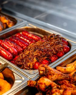 Bac de saucisses grillées avec oignons caramélisés et morceaux de poulet rôti dans un restaurant rôtisserie.