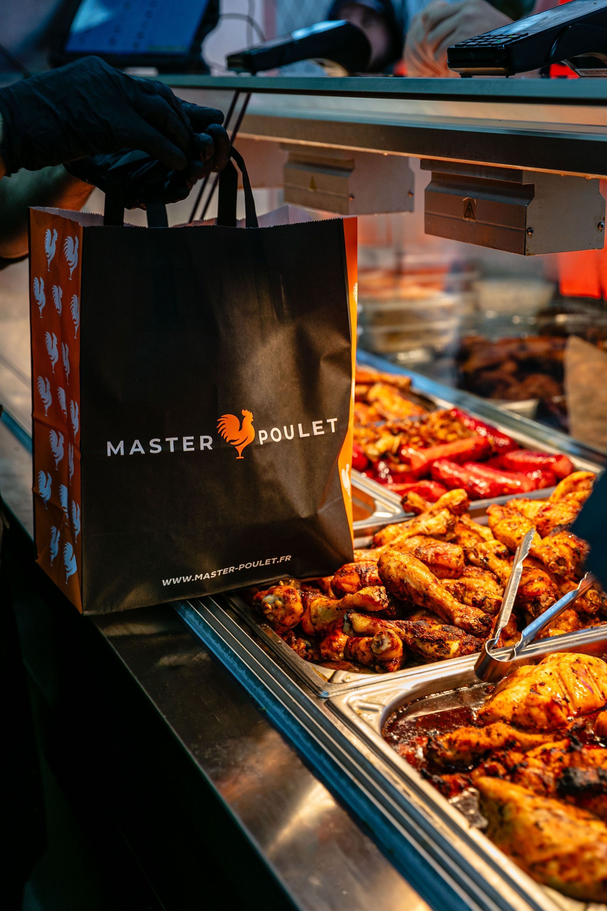 Sac à emporter Master Poulet posé à côté d'un buffet de poulets grillés et rôtis dans un restaurant à Boulogne-Billancourt.