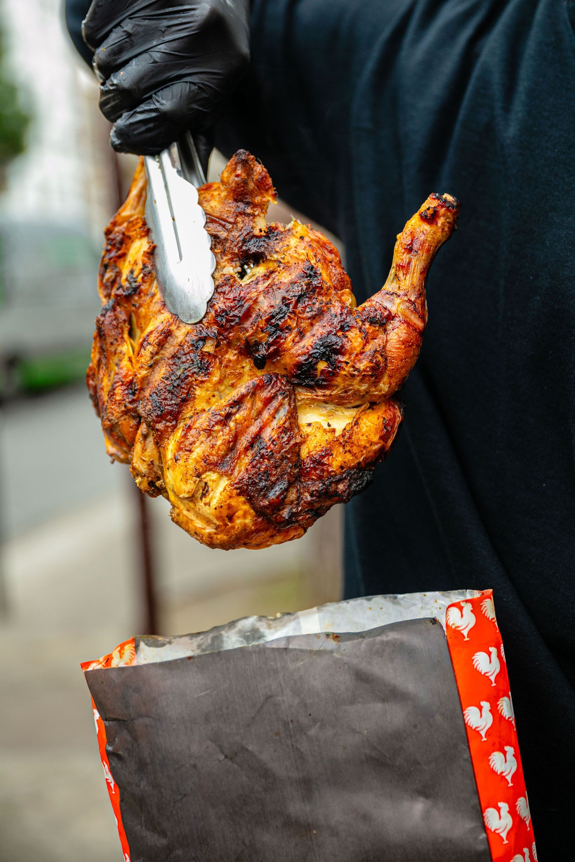 Poulet grillé tenu avec une pince, prêt à être mis dans un sac de restaurant à emporter.