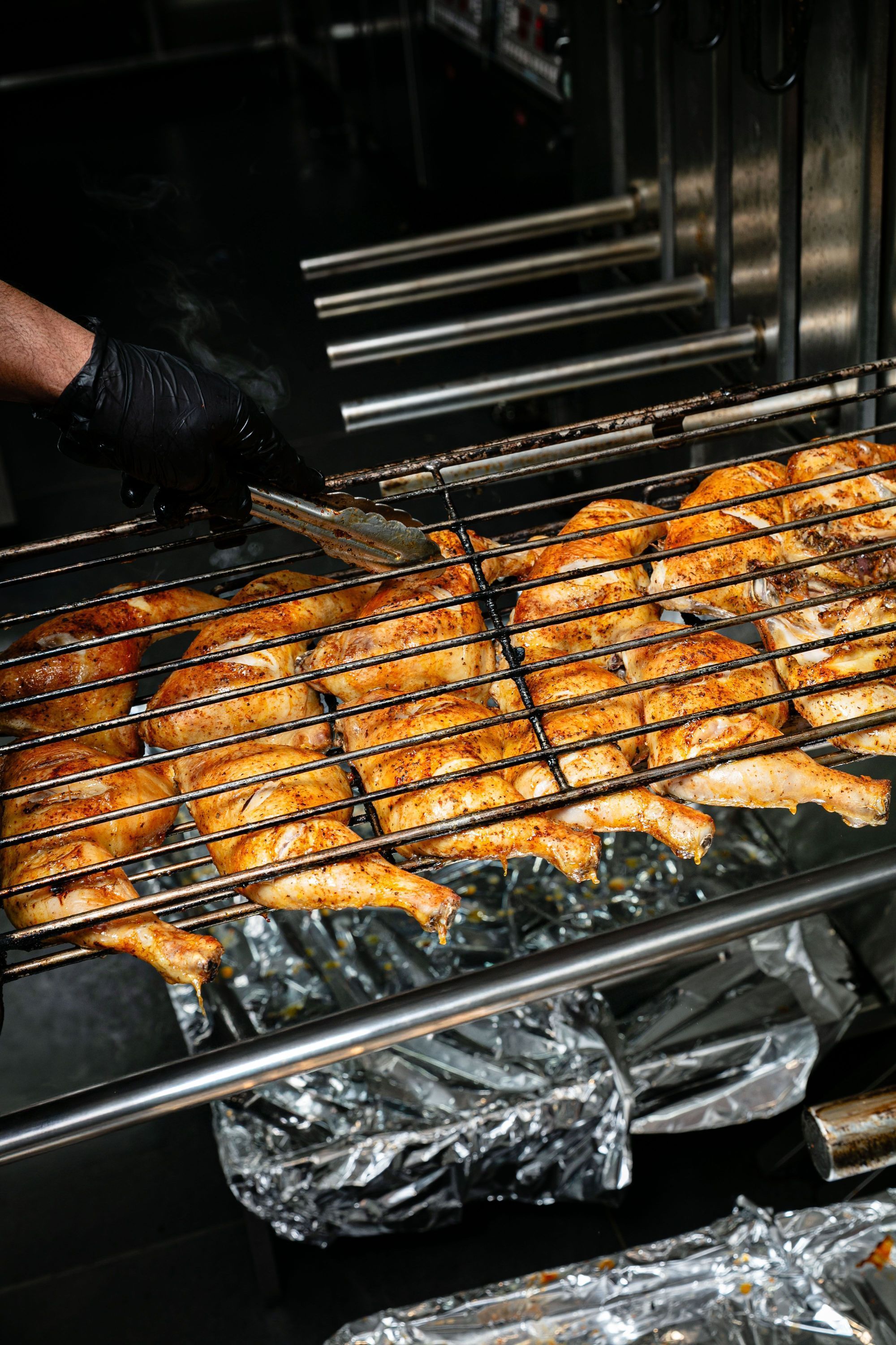 Poulets grillés en rôtisserie dans un restaurant, en cuisson sur une grille métallique, vus de côté.