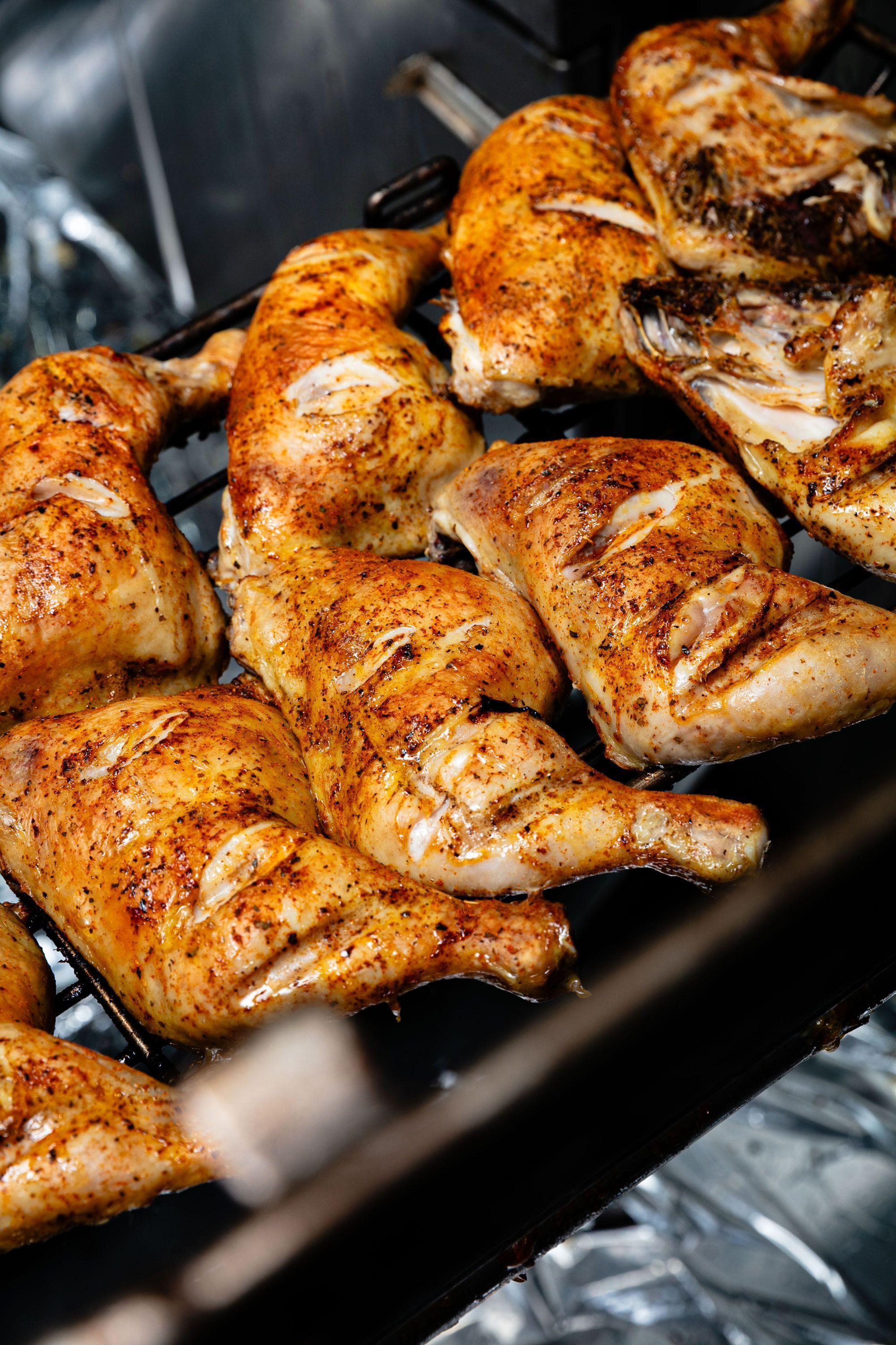Poulets rôtis bien dorés cuisant sur une grille dans un restaurant rôtisserie, texture peau croustillante et épices visibles.