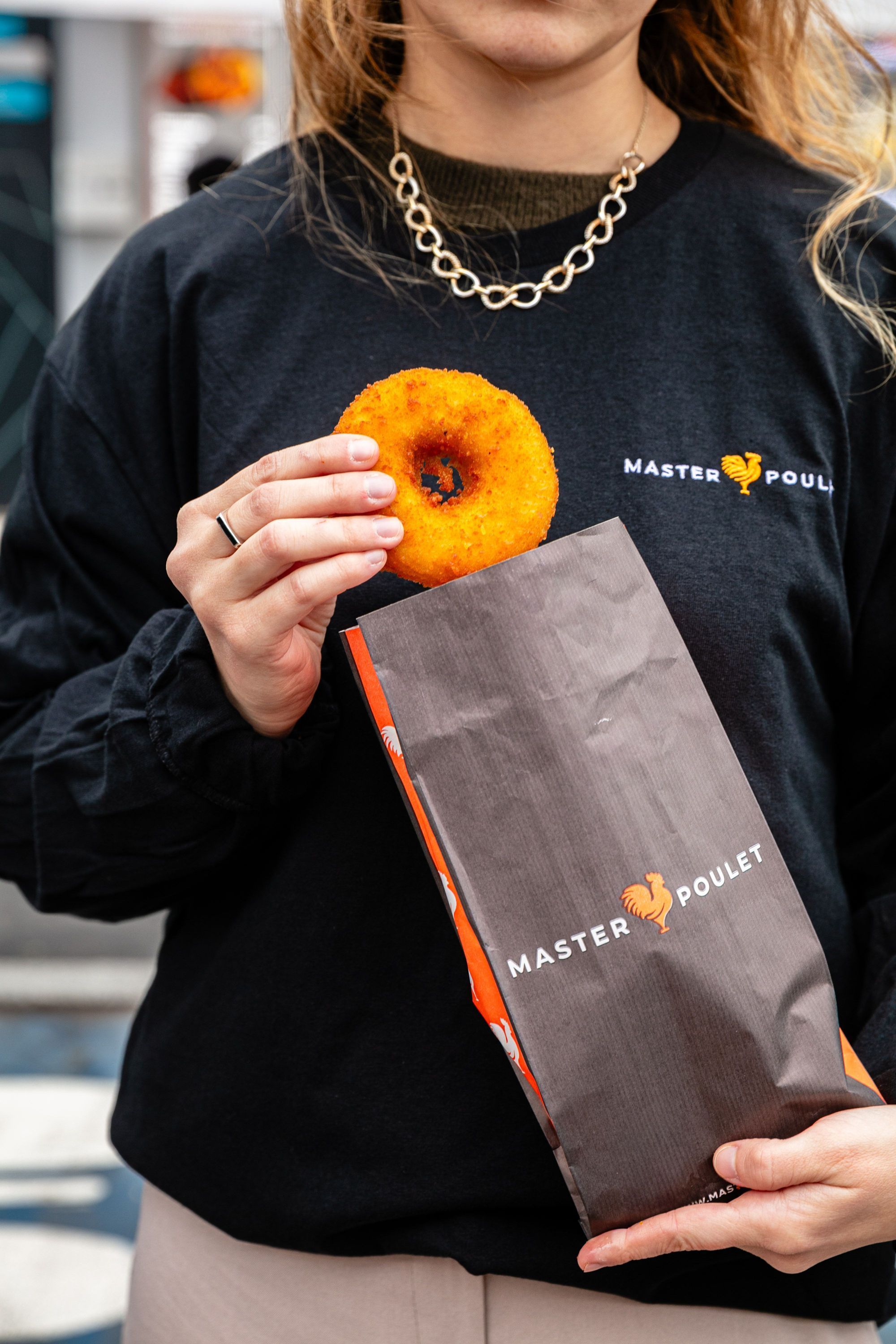 Sac à emporter Master Poulet avec une personne tenant un beignet, vêtue d'un sweat noir avec logo du restaurant